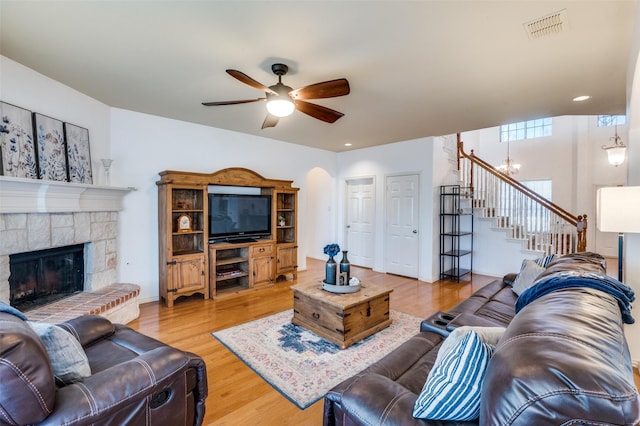 living room featuring ceiling fan with notable chandelier, hardwood / wood-style floors, and a stone fireplace