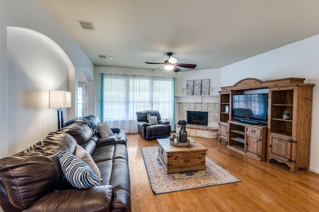 living room with ceiling fan, light hardwood / wood-style flooring, and a stone fireplace