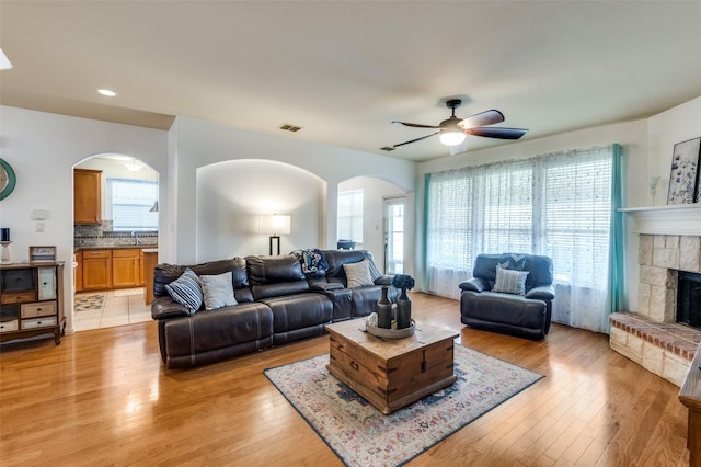 living room featuring ceiling fan, sink, light wood-type flooring, and a fireplace