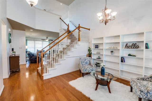 sitting room with ceiling fan with notable chandelier, hardwood / wood-style flooring, and a towering ceiling