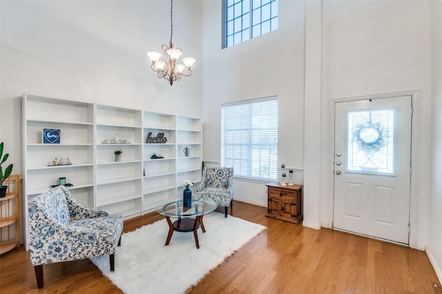 living area with a towering ceiling, a chandelier, and light wood-type flooring