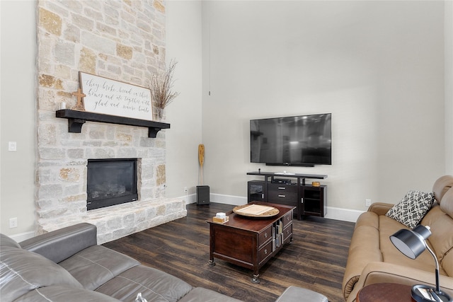 living room featuring a stone fireplace, baseboards, and wood finished floors