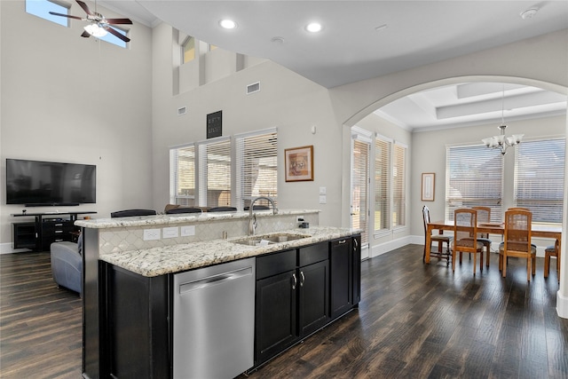 kitchen with arched walkways, a sink, open floor plan, dark cabinetry, and dishwasher