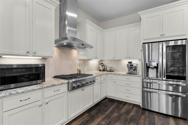 kitchen with dark wood finished floors, wall chimney exhaust hood, appliances with stainless steel finishes, white cabinetry, and backsplash