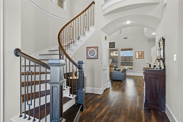 entryway featuring visible vents, baseboards, arched walkways, a towering ceiling, and hardwood / wood-style flooring