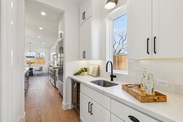 kitchen with white cabinets, stainless steel range, decorative backsplash, sink, and light wood-type flooring