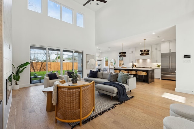 living room with ceiling fan, a high ceiling, and light hardwood / wood-style floors