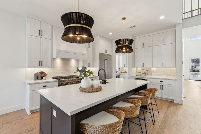 kitchen with range, white cabinets, a center island with sink, and backsplash