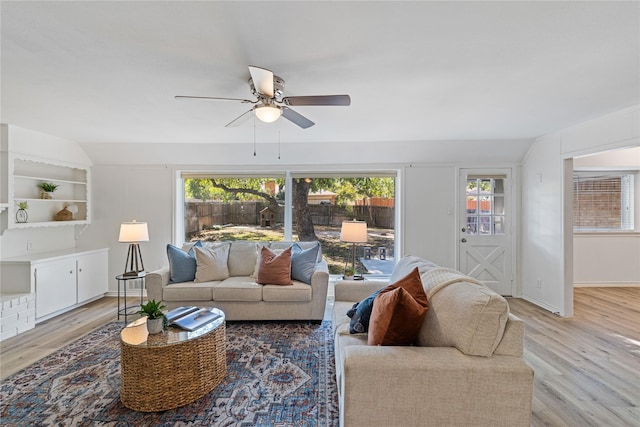 living room with built in features, light hardwood / wood-style flooring, ceiling fan, and vaulted ceiling