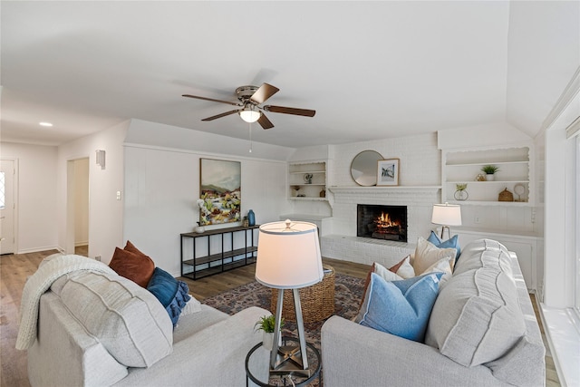 living room with ceiling fan, lofted ceiling, a fireplace, wood-type flooring, and built in features