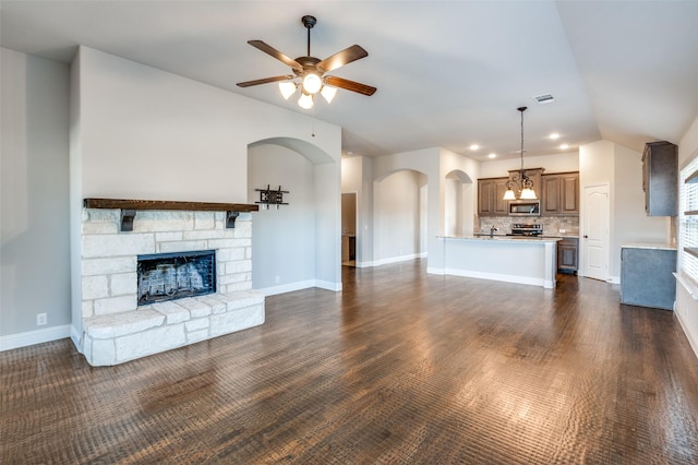 unfurnished living room with a stone fireplace, vaulted ceiling, dark hardwood / wood-style floors, and ceiling fan