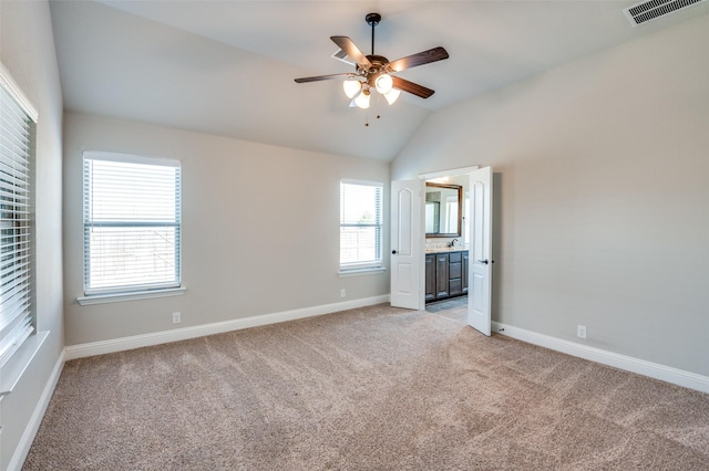 unfurnished bedroom with ceiling fan, ensuite bathroom, vaulted ceiling, and light carpet