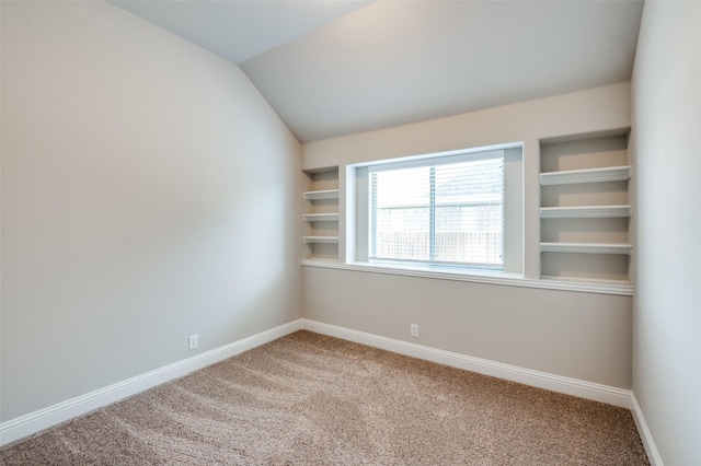 empty room featuring lofted ceiling, built in shelves, and carpet flooring