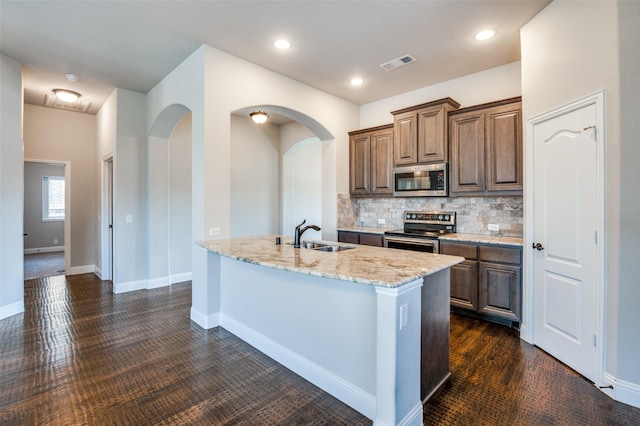 kitchen with sink, a center island with sink, appliances with stainless steel finishes, light stone countertops, and backsplash