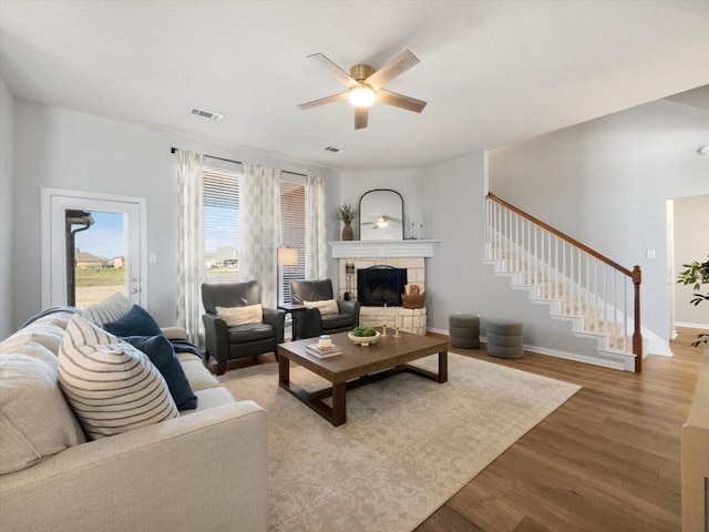 living room featuring ceiling fan, wood-type flooring, and a stone fireplace