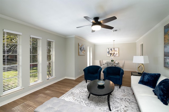 living room with ceiling fan with notable chandelier, plenty of natural light, and crown molding