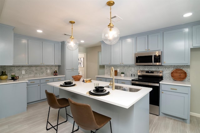 kitchen featuring pendant lighting, stainless steel appliances, decorative backsplash, sink, and a kitchen island with sink