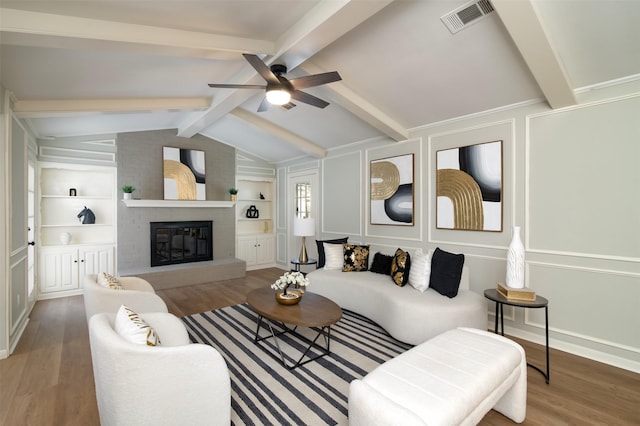 living room featuring ceiling fan, a fireplace, lofted ceiling with beams, wood-type flooring, and built in shelves