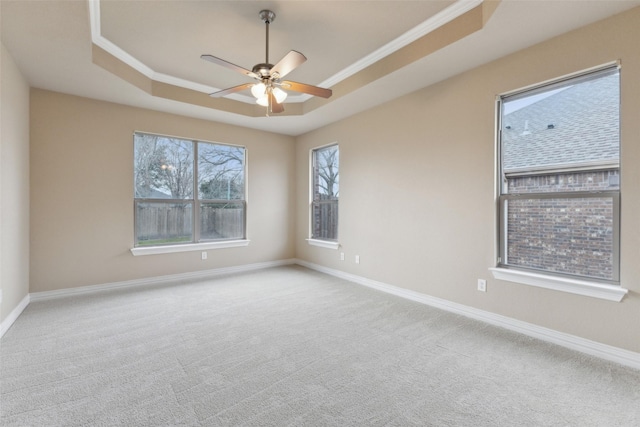 carpeted spare room with ceiling fan, plenty of natural light, a tray ceiling, and ornamental molding