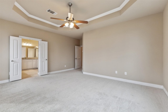 unfurnished bedroom with ceiling fan, light colored carpet, connected bathroom, and a tray ceiling