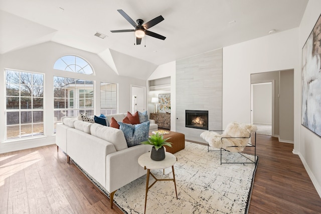 living room with ceiling fan, dark wood-type flooring, a tile fireplace, and lofted ceiling