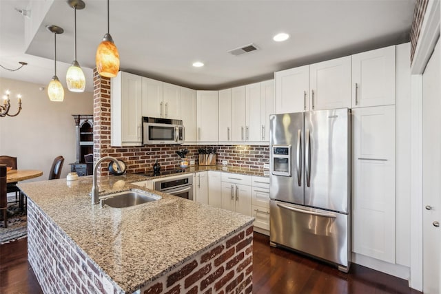 kitchen featuring white cabinetry, appliances with stainless steel finishes, decorative light fixtures, light stone counters, and sink