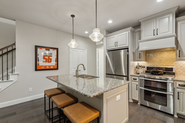 kitchen with appliances with stainless steel finishes, sink, hanging light fixtures, light stone counters, and a center island with sink