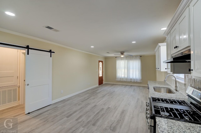 kitchen featuring white cabinetry, a barn door, gas stove, light stone countertops, and sink