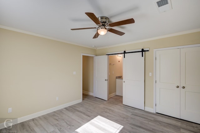 unfurnished bedroom featuring ceiling fan, a barn door, light hardwood / wood-style floors, ornamental molding, and a closet