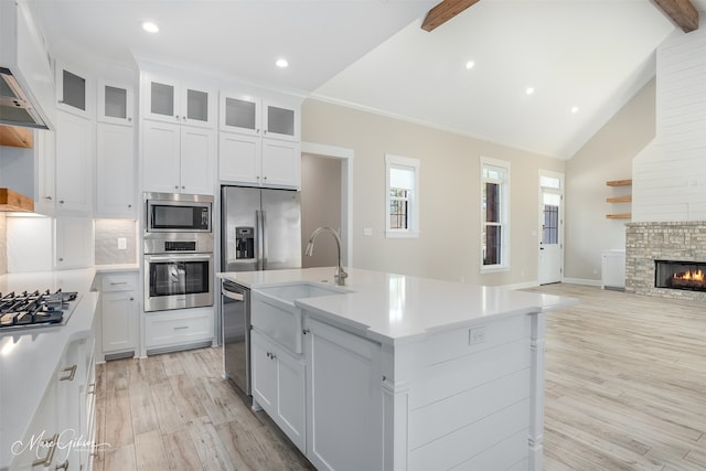 kitchen with custom exhaust hood, white cabinets, appliances with stainless steel finishes, and an island with sink