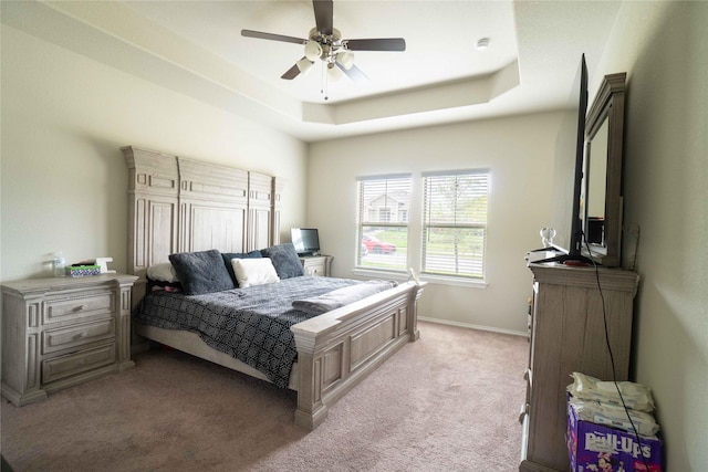 bedroom with light colored carpet, baseboards, a tray ceiling, and ceiling fan