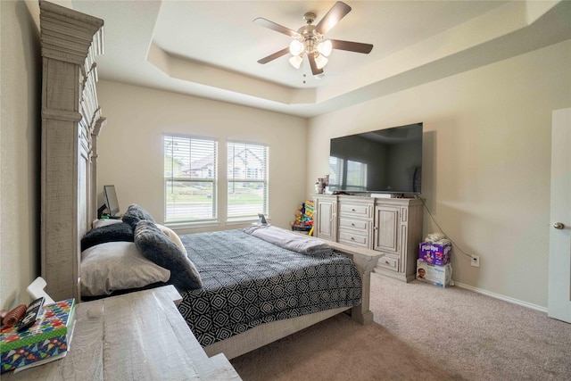 bedroom with a tray ceiling, baseboards, light colored carpet, and ceiling fan