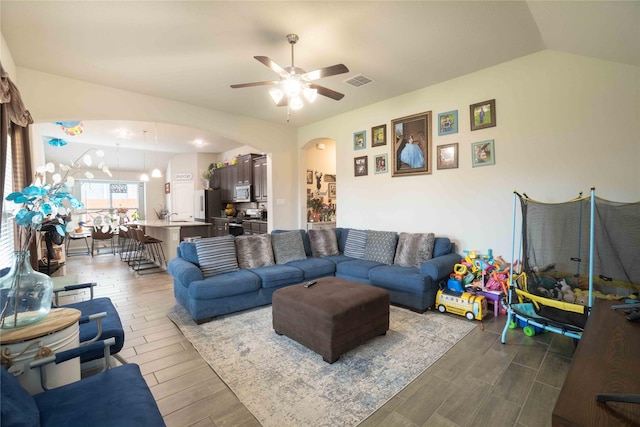 living area with a ceiling fan, visible vents, wood finish floors, lofted ceiling, and arched walkways