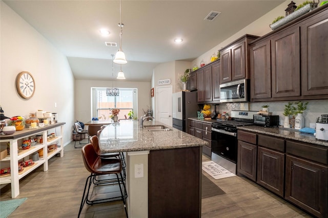 kitchen featuring a center island with sink, stainless steel appliances, visible vents, and a breakfast bar