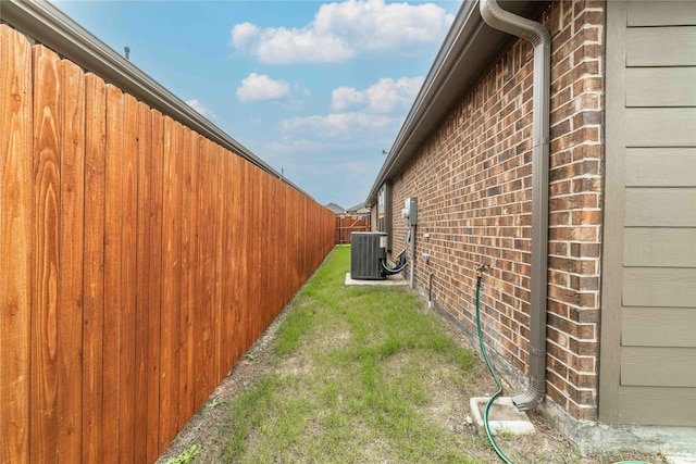 view of side of home featuring central air condition unit, brick siding, a lawn, and fence