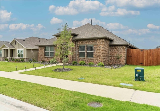 view of front of property featuring a front yard, fence, brick siding, and roof with shingles