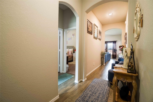 hallway featuring wood finish floors, baseboards, arched walkways, and a textured wall