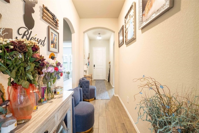 hallway with baseboards, arched walkways, and light wood-type flooring