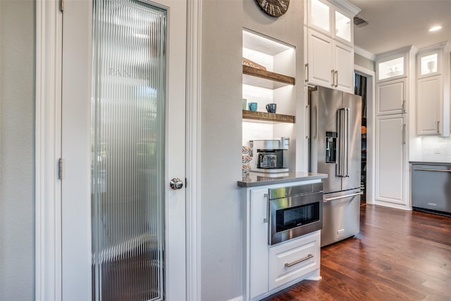 kitchen with appliances with stainless steel finishes, dark wood-type flooring, white cabinetry, and decorative backsplash