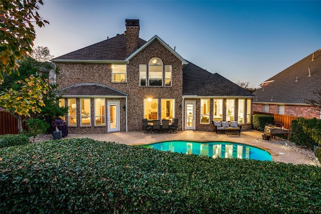 back house at dusk featuring a patio area, outdoor lounge area, and a fenced in pool