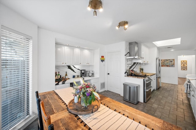 kitchen featuring a skylight, wall chimney exhaust hood, stainless steel appliances, and white cabinetry