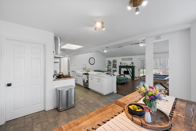 kitchen featuring billiards, kitchen peninsula, stainless steel gas cooktop, a skylight, and white cabinets