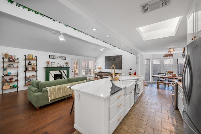 kitchen with vaulted ceiling with skylight, stainless steel refrigerator, a kitchen breakfast bar, an island with sink, and white cabinets