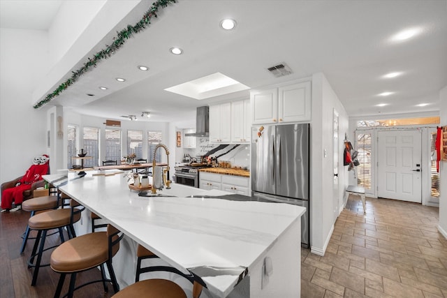 kitchen featuring wall chimney range hood, a kitchen bar, white cabinetry, appliances with stainless steel finishes, and a large island