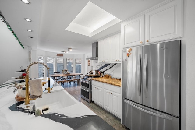 kitchen featuring wall chimney exhaust hood, white cabinetry, a skylight, stainless steel appliances, and tasteful backsplash