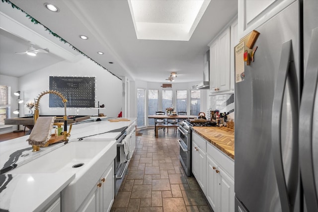 kitchen with ceiling fan, decorative backsplash, white cabinetry, stainless steel appliances, and wall chimney exhaust hood