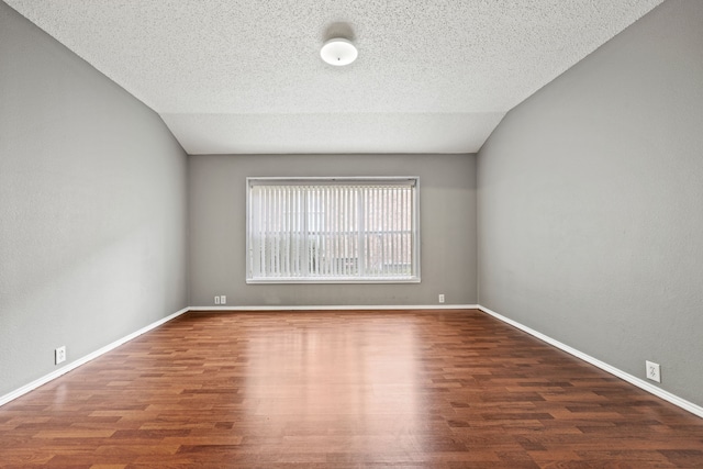 spare room with dark wood-type flooring, a textured ceiling, and vaulted ceiling