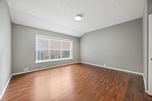 empty room with lofted ceiling, dark hardwood / wood-style floors, and a textured ceiling