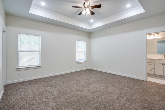 unfurnished bedroom with light colored carpet, a tray ceiling, and ensuite bath