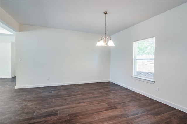 spare room featuring dark wood-type flooring and a chandelier